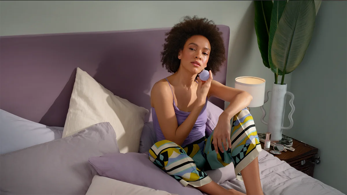 A woman sitting on a bed, doing a microcurrent facial lifting with BEAR 2 mini 